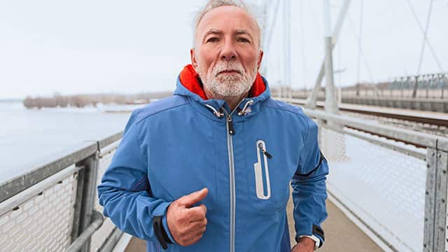 A senior man in a blue coat is running on the bridge