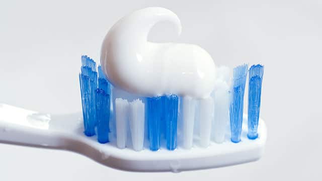 A close up of white the toothpaste on a white toothbrush with blue and white bristles