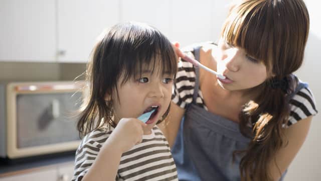 a mother and a daughter brushing their teeth with Colgate tootbrush