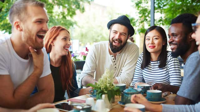 A group of friends smiling and talking at an outdoor table.