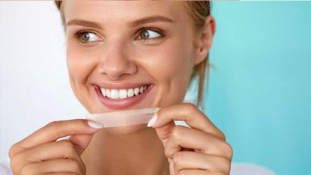 Young woman using teeth whitening strips.
