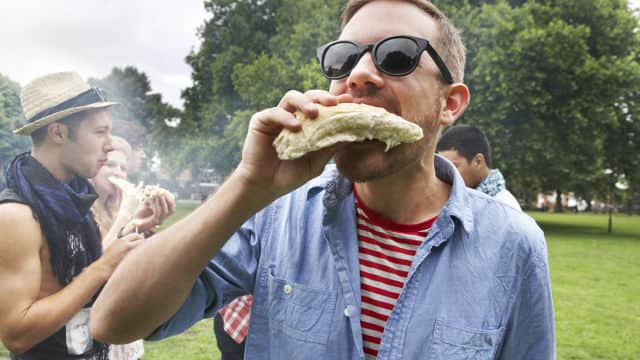 a group of people gathered outdoor smiling while eating