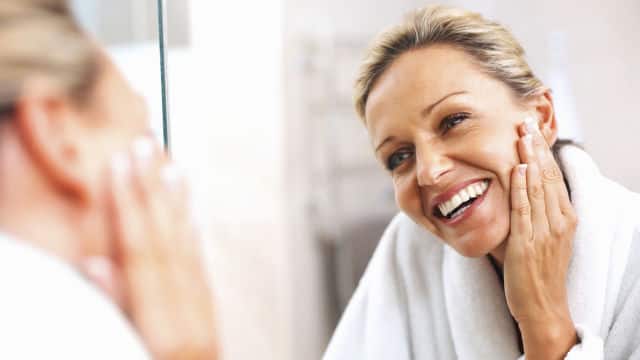 A women with her hand of her cheek and similling while looking at a mirror