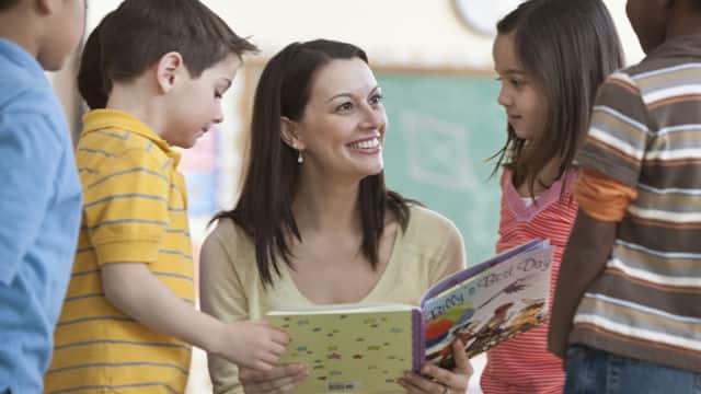 a teacher smiling showing a book to a group of children
