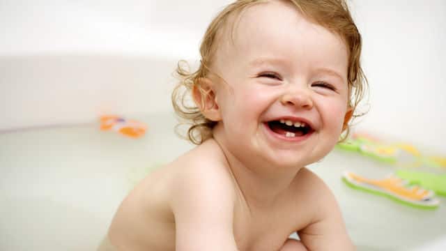 a teething baby is taking a bath with first tooth erupted