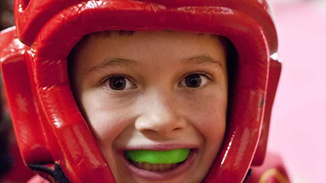 young boy smiling wearing a head protective gear and a mouth guard