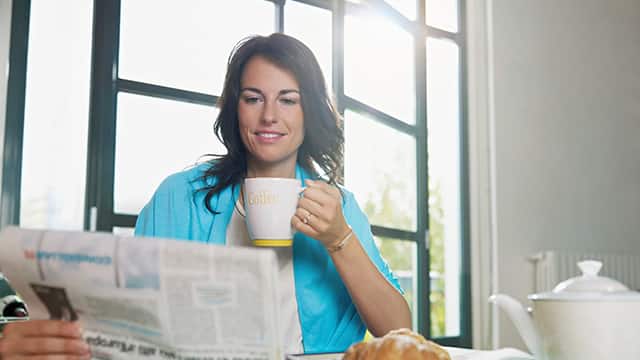 a woman drinking coffee while reading the newspaper