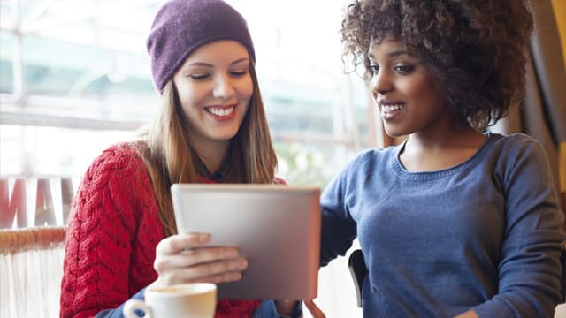 two girls looking at ipad together in a coffee shop