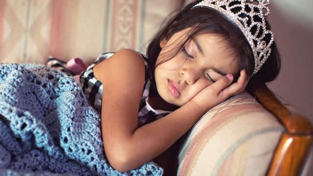 a girl wearing a tiara sleeping on the couch