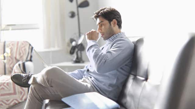 Señor sentado en el sofá leyendo mientras toma café