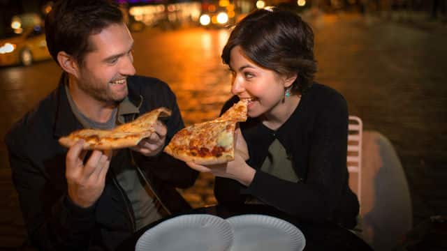 a young couple eating pizza outdoors