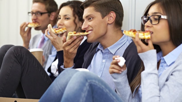 a group of people sitting down enjoying a slice of pizza