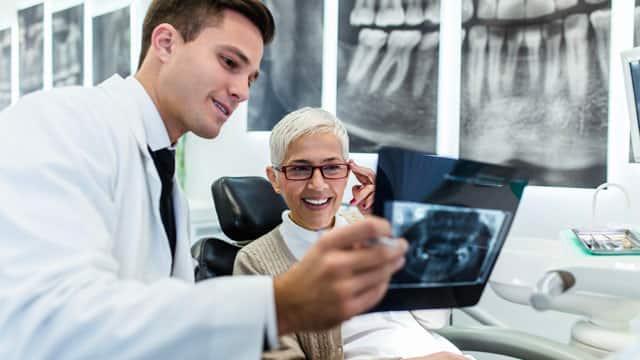 A male dentist and a female patient examining an X-ray image of her teeth.