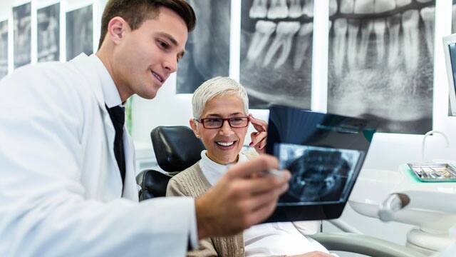 A male dentist and a female patient examining an X-ray image of her teeth. A male dentist and a female patient examining an X-ray image of her teeth.