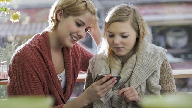 A blonde woman with her friend smiling while looking at her phone