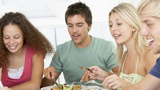 two men and two women smiling while enjoying their food