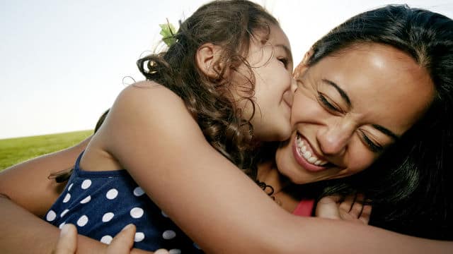 a girl kissing her mother on the cheek, and the mother is smiling brightly