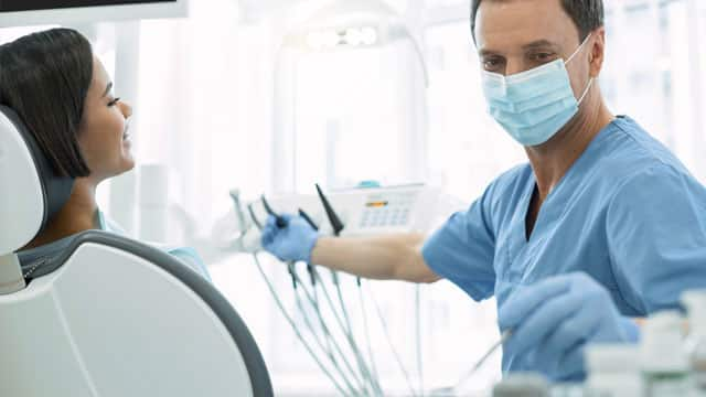 A male dentist with a mask and gloves examining a patient.