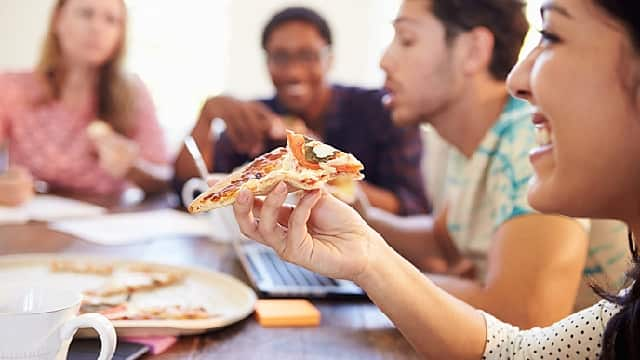 a group of people smiling and laughing while enjoying pizza