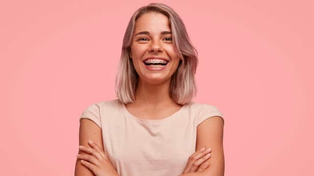 woman with braces smiling brightly with her arm crossed