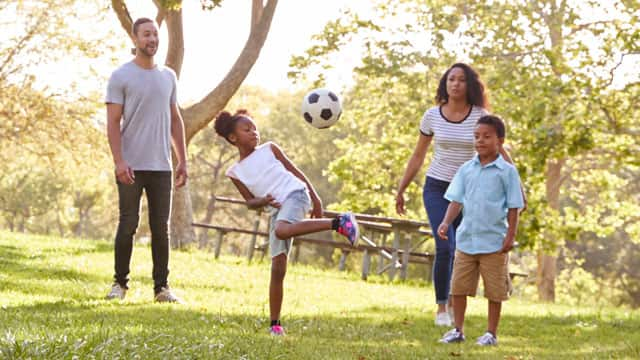 A family playing with a soccer ball in the park.