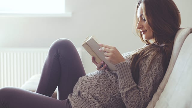 Pregnant woman smiling while reading a book