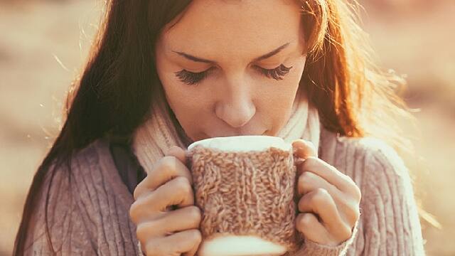 A girl is drinking hot beverage to ease discomfort of sore throat and tongue