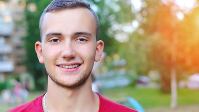 A young man outside smiling wearing ceramic braces.