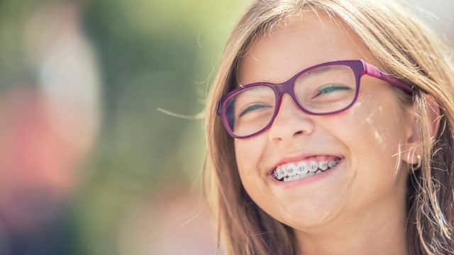 A young girl smiling with braces outside.
