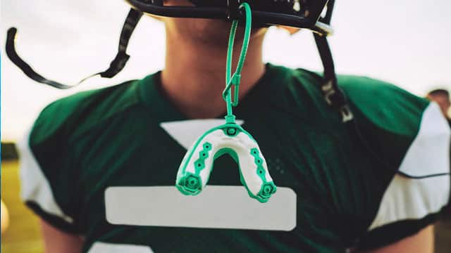 An American football player with a mouthguard hanging from their helmet. 