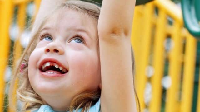 A young, smiling girl with missing teeth playing on monkey bars.