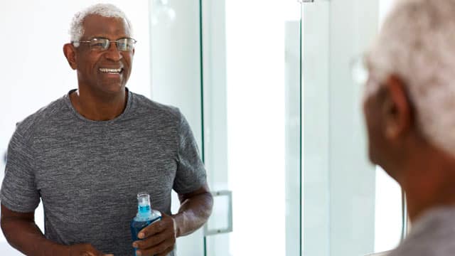 A senior man using mouthwash in a bathroom.