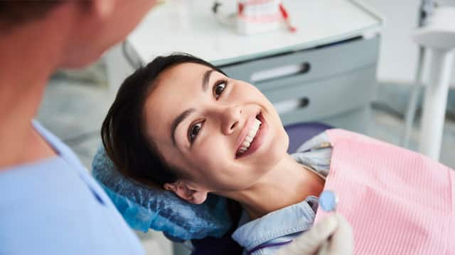 A woman is sitting in a dental armchair while getting her teeth examined.