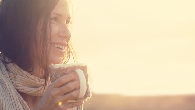 Mujer tomando una bebida caliente mientras sonrie
