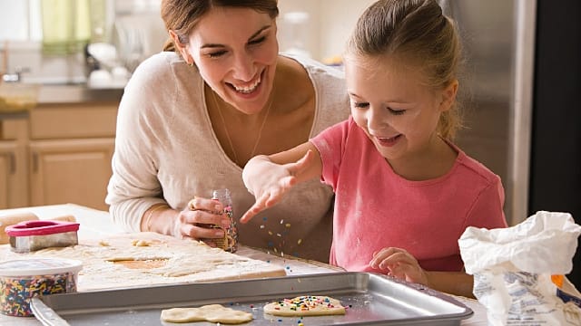 A young girl is baking cookies with her mother in the kitchen