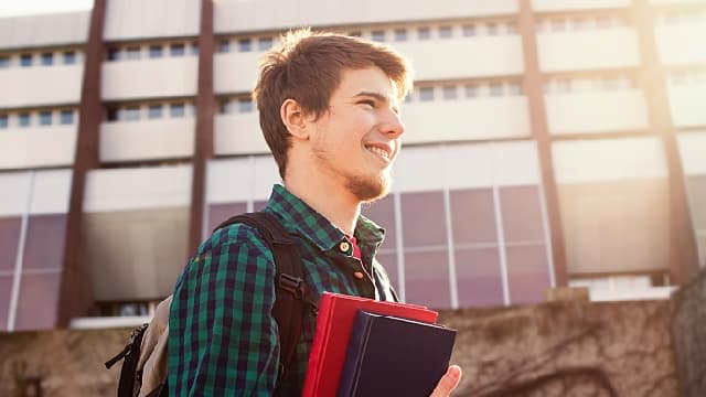 Young college boy holding books on campus