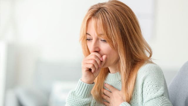 A woman coughing while covering her mouth and holding her chest