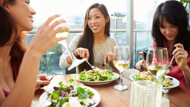 Three happy women eating salads and drinking wine