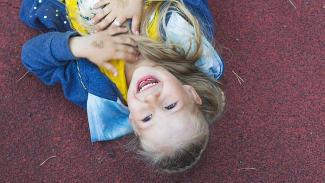 Little girl playing and laying on the ground with a toothless smile.