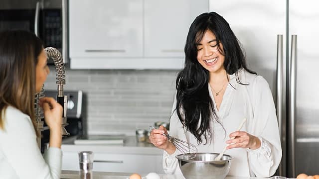 two women in the kitchen smiling brightly cooking