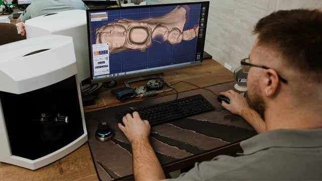 A person working at a computer in a dental laboratory for prosthesis and crown milling.