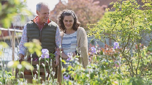 an elderly couple smiling at the garden enjoying a stroll