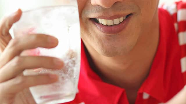 A close up of a man holding a glass with sparkling water and ice