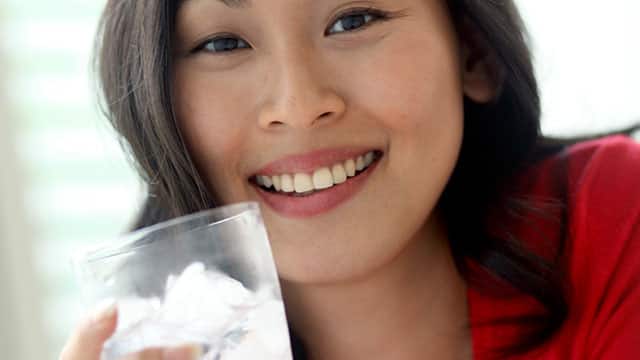 A woman is holding a glass with ice water