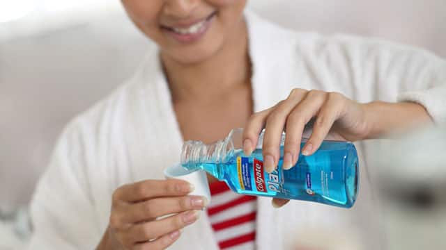 A close up of the woman using a Colgate mouthwash