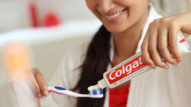 Young woman squeezing Colgate toothpaste on a toothbrush