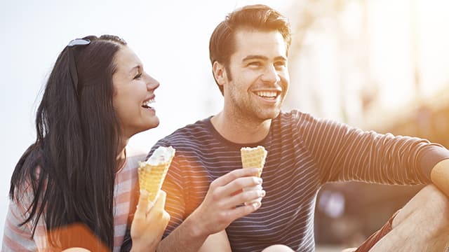 man and a woman laughing while enjoying an ice cream cone outdoor