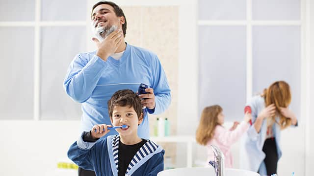 a father applying shaving cream while the son is brushing his teeth with Colgate toothbrush