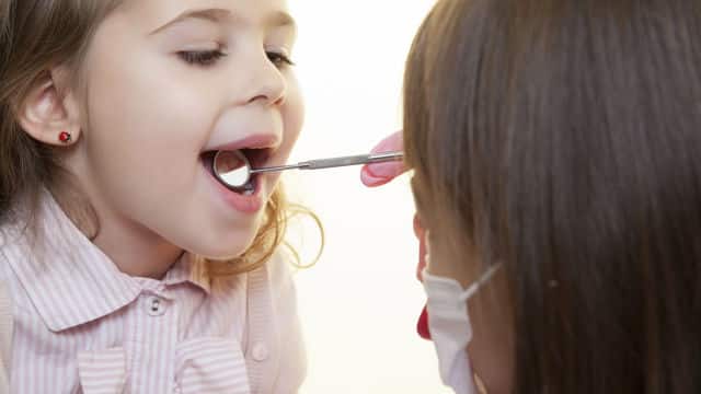 a dentist using a dental mirror on a girl mouth