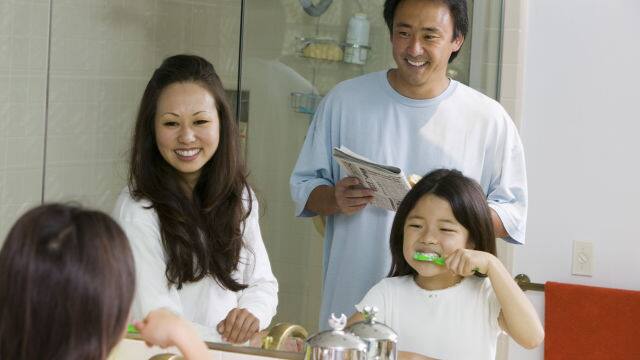 a father and mother watching their child brushing her teeth with Colgate toothbrush